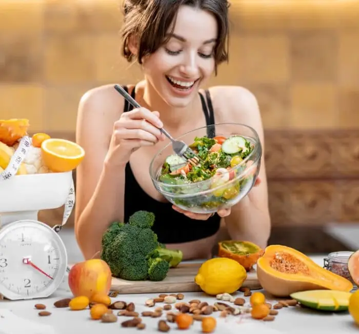 A person eating a bowl of salad surrounded by fresh fruit and vegetables